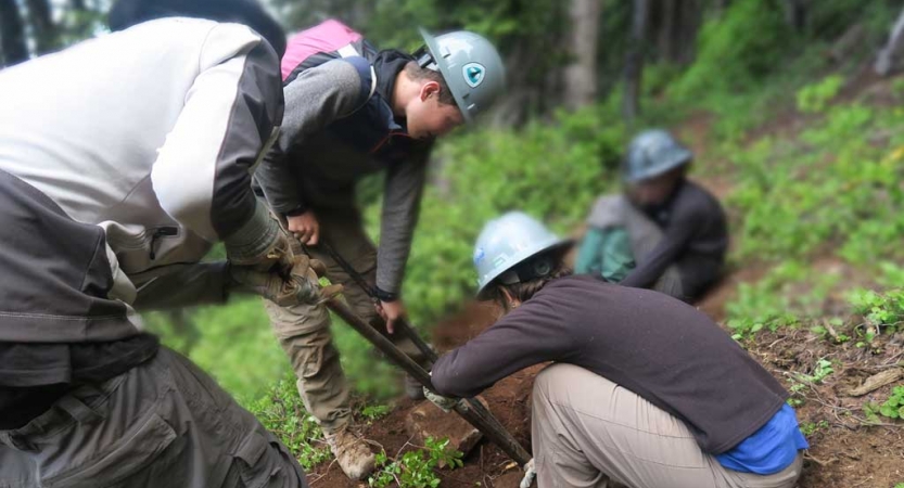 A group of students use gardening tools during a service project with outward bound